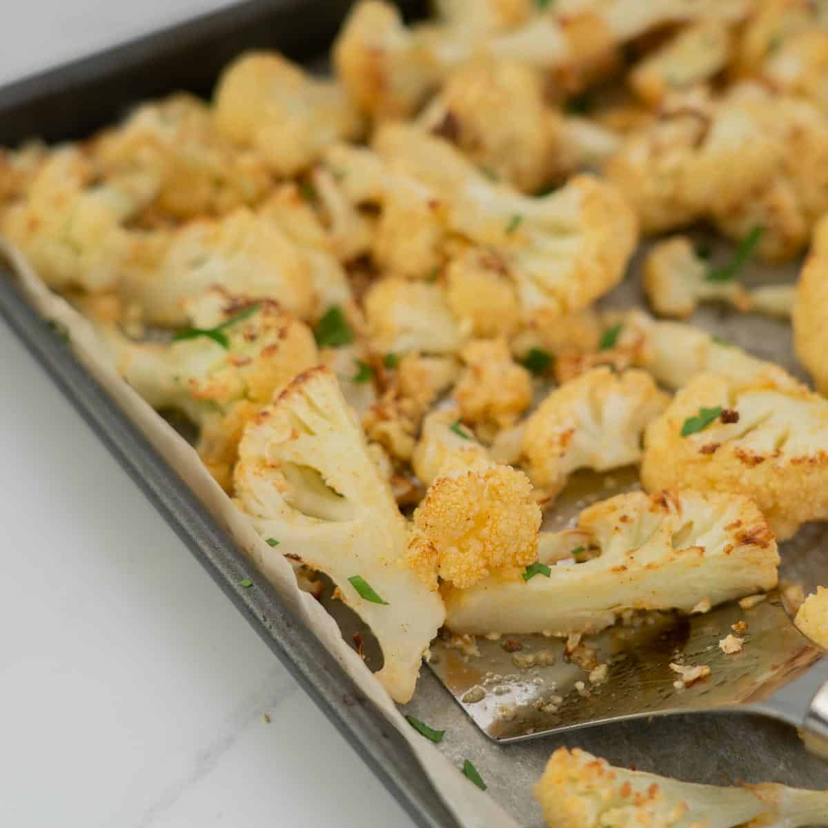 golden roast cauliflower sprinkled with a little chop parsely in a roasting pan. 