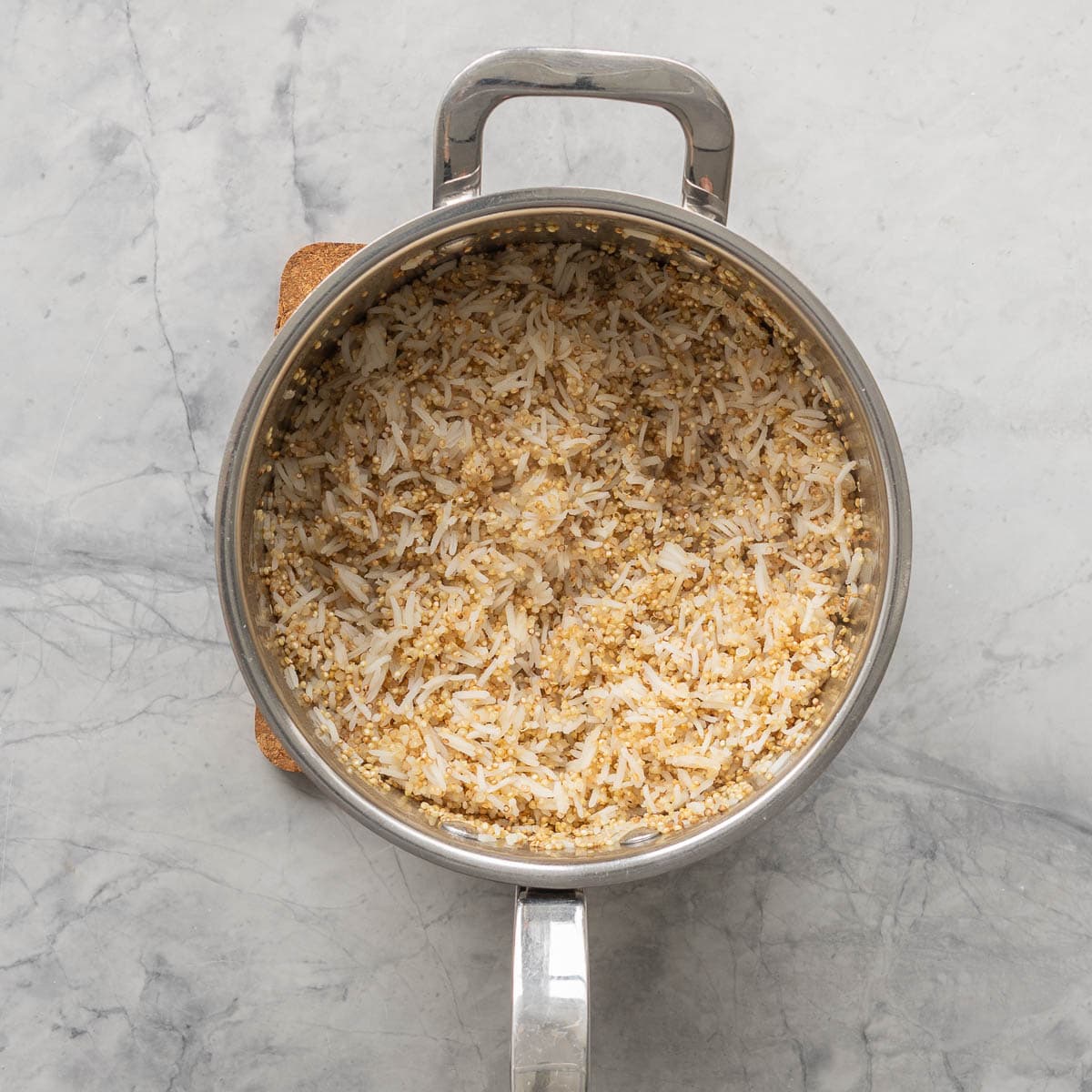 Cooked quinoa and rice in a saucepan sitting on a grey marble bench. 